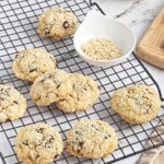 Wire rack with sesame-coated cookies, small bowl of sesame seeds, and bowl of chocolate chips in the background.