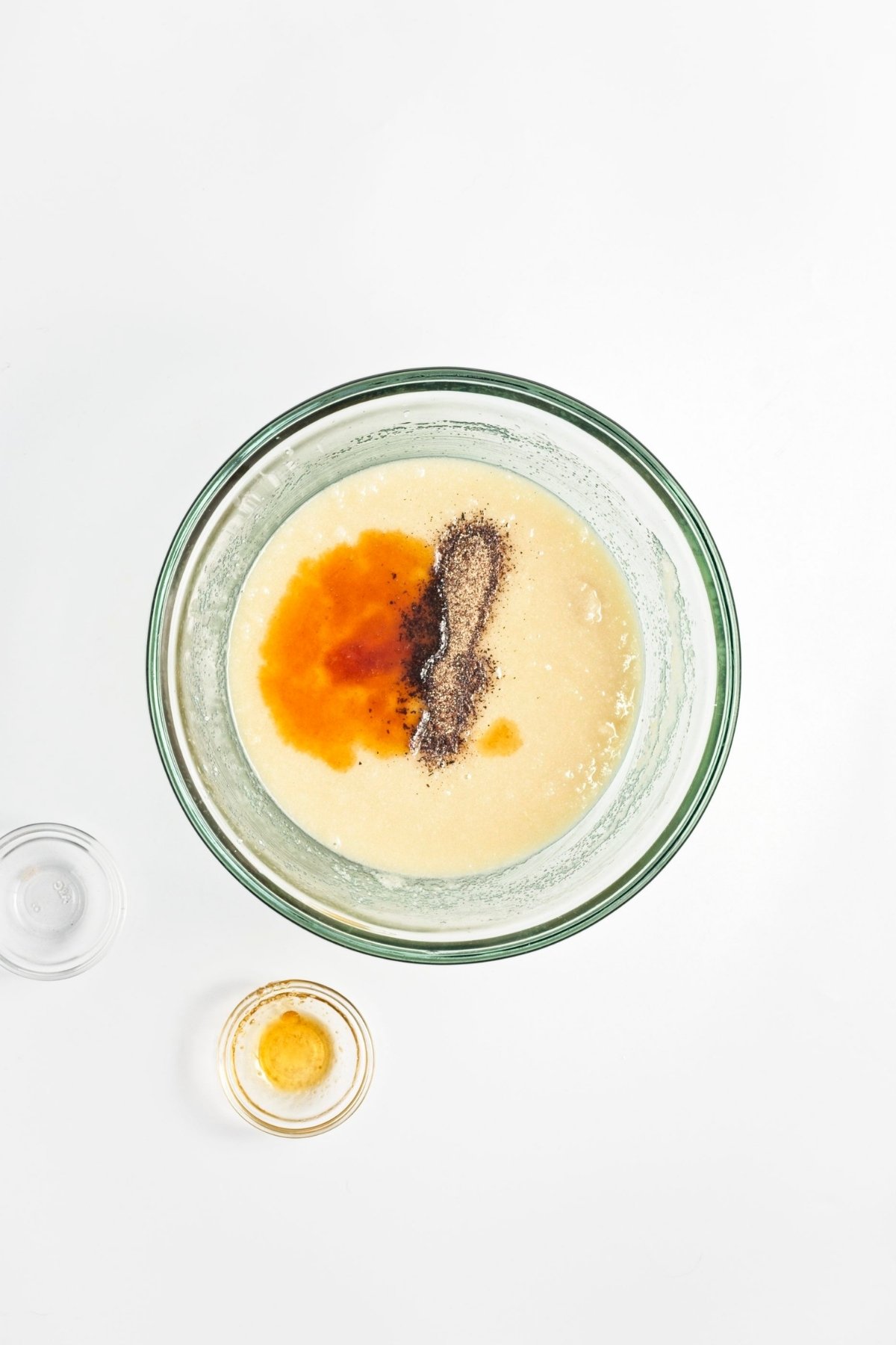 Mixing bowl with blended wet mixture topped with toasted sesame oil and ground cardamom.