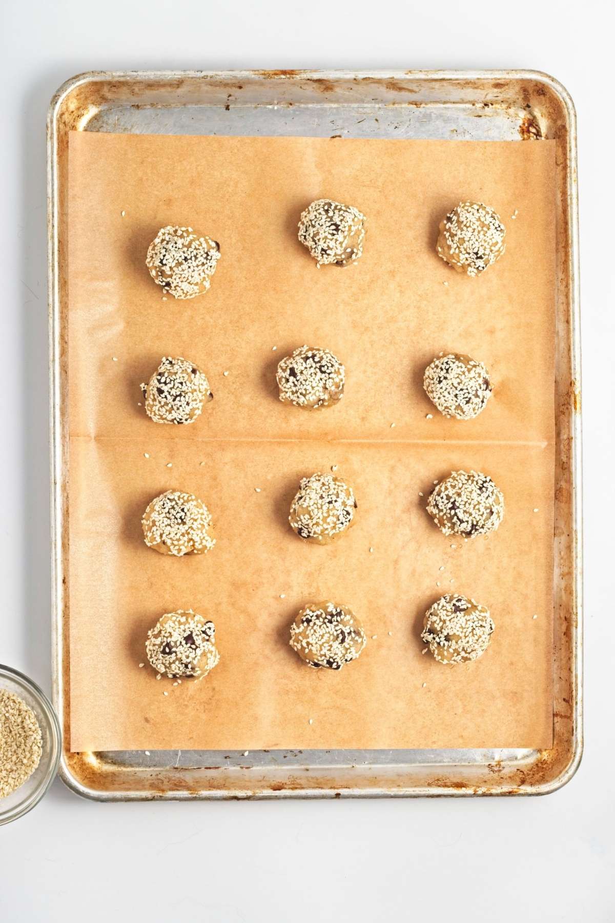 Baking sheet with sesame-coated cookie dough balls spaced evenly on parchment.