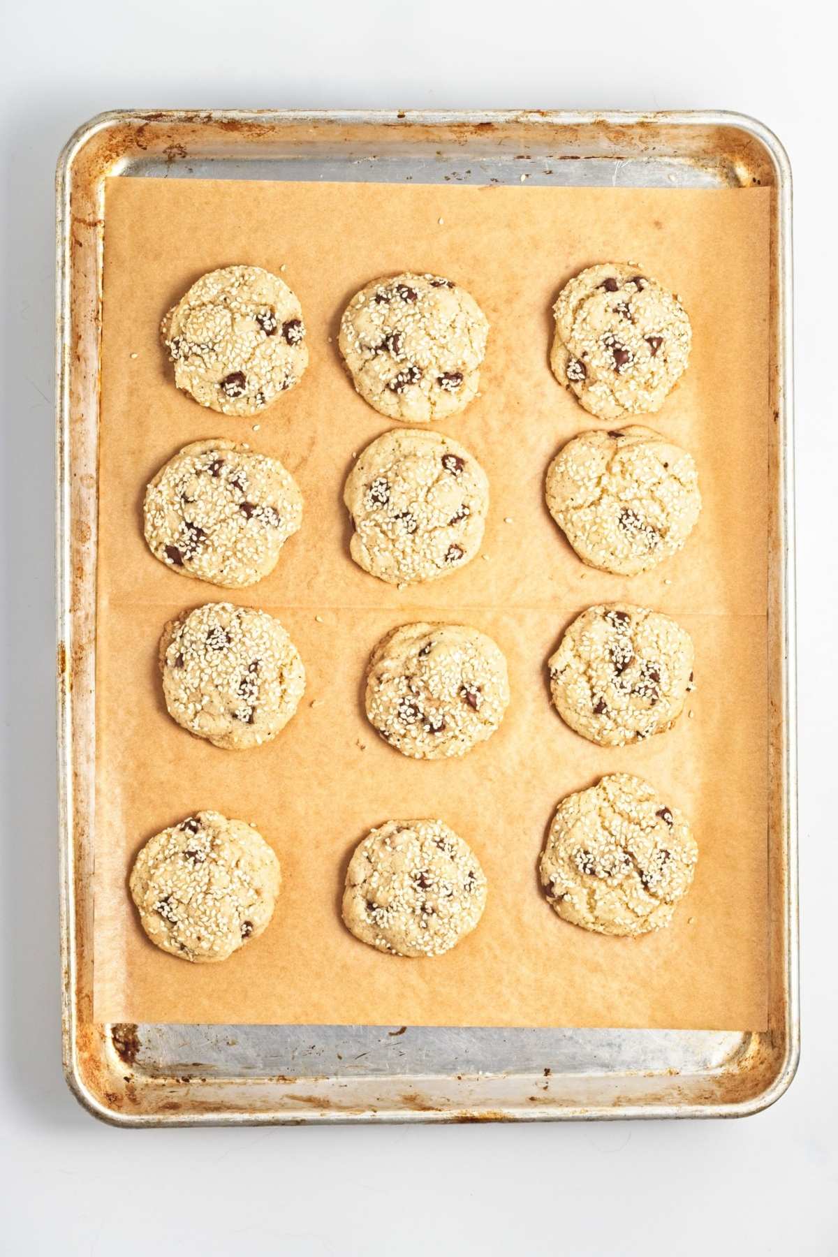 Baked cookies with sesame seed tops cooling on a parchment-lined baking sheet.