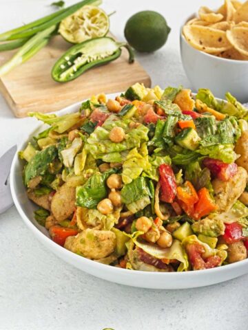 Large bowl of chopped lettuce, chickpeas, tomatoes, cucumber, and tortilla chips tossed together.