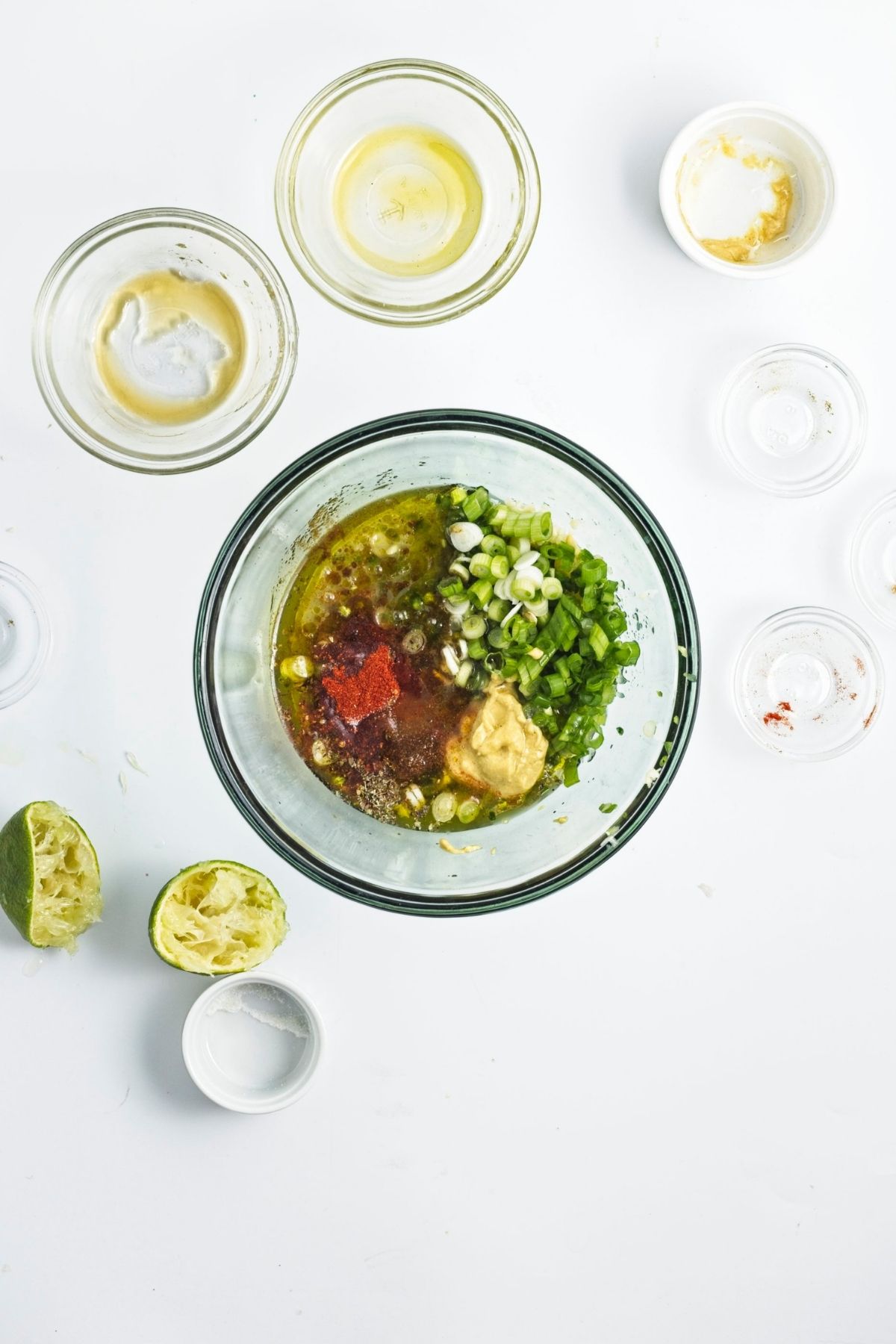 Bowl of whisked dressing with chopped green onions and herbs.