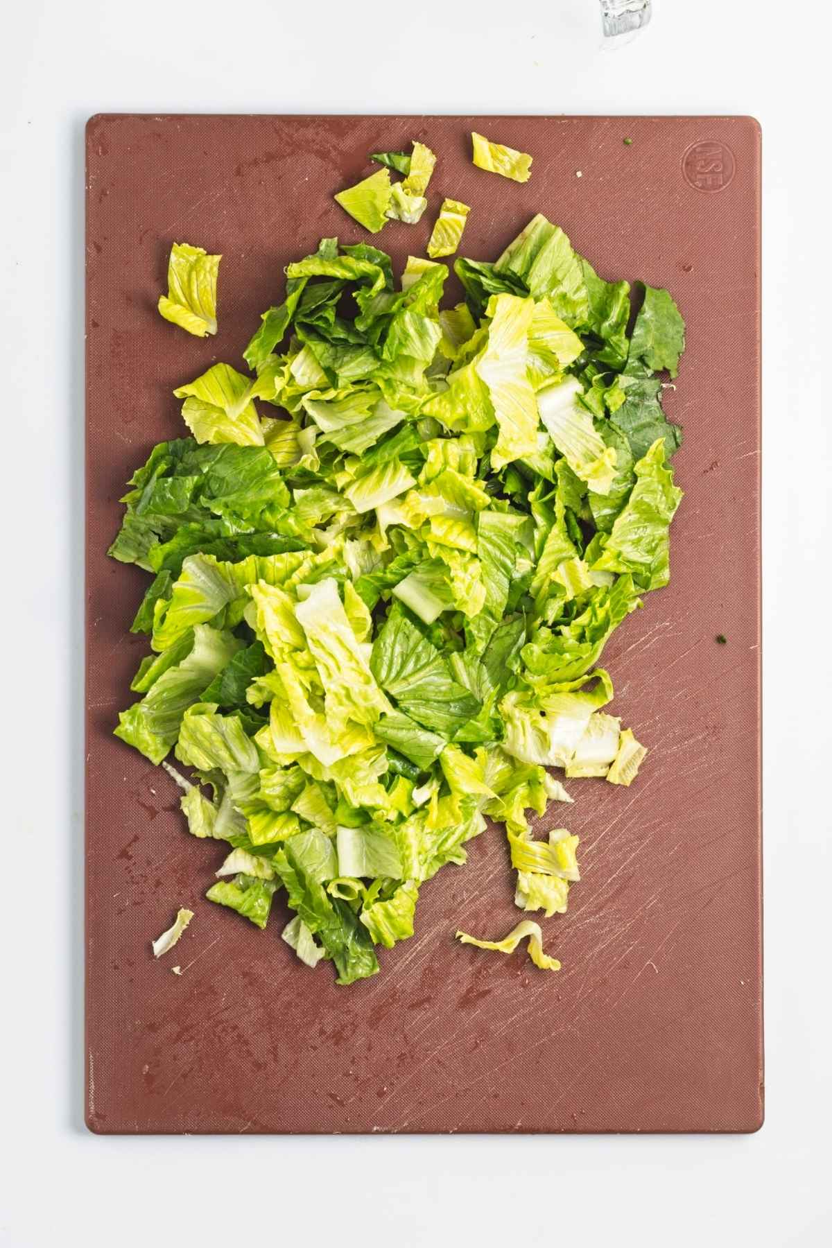 Chopped romaine lettuce on a brown cutting board.