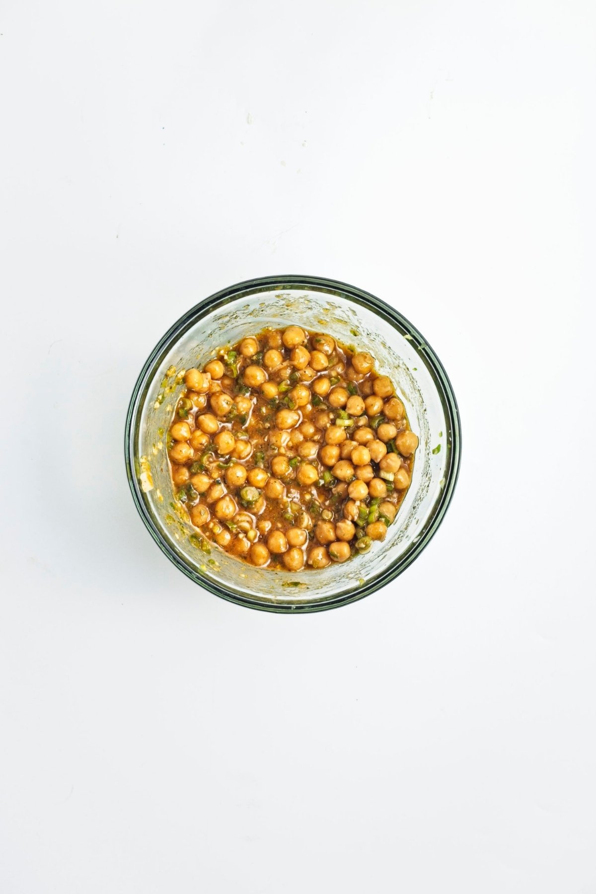 Chickpeas marinating in dressing in a glass bowl.