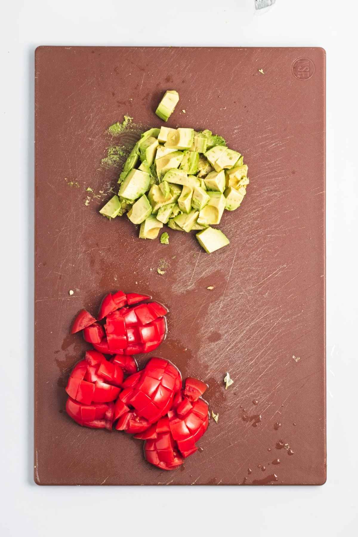 Diced avocado and chopped tomatoes on a brown cutting board.