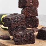 Stack of moist brownies with visible chocolate chunks on a wooden board.