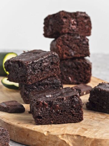 Stack of moist brownies with visible chocolate chunks on a wooden board.