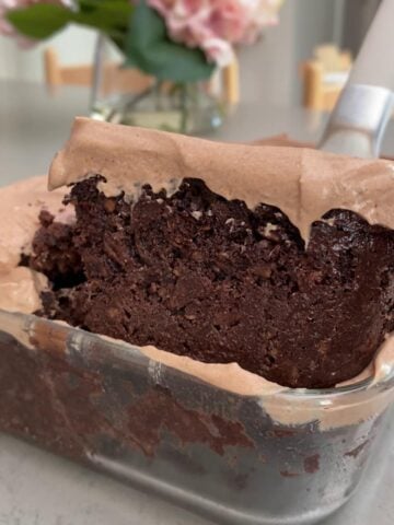 Slice of fudgy chocolate oats with creamy yogurt frosting being lifted from glass dish.