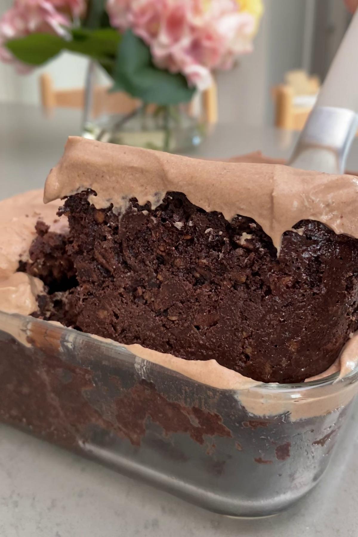Slice of fudgy chocolate oats with creamy yogurt frosting being lifted from glass dish.