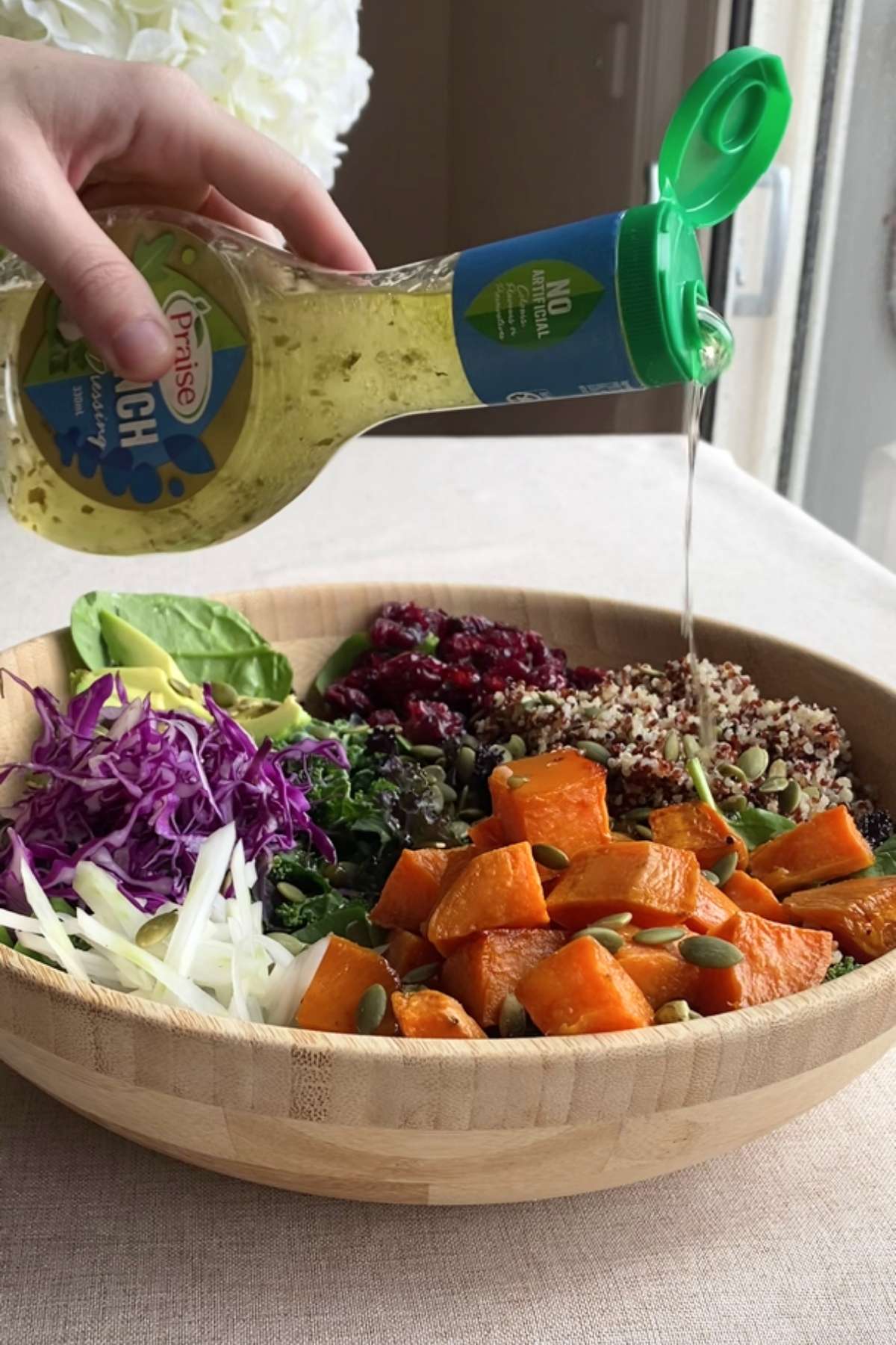 Dressing being poured over salad with kale, quinoa, sweet potato, and cabbage.