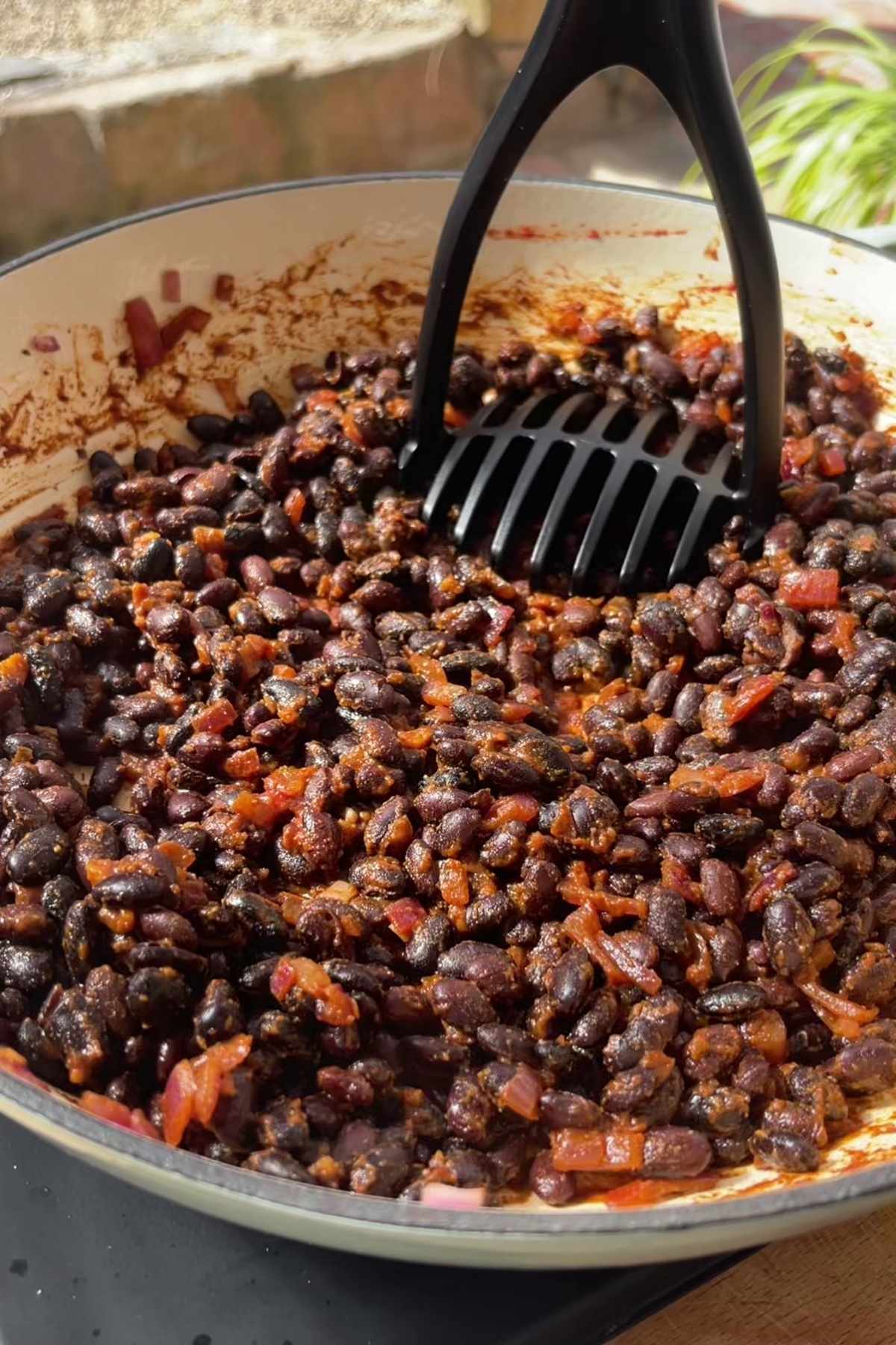 Black beans simmered with tomato and spices being mashed in a pan.