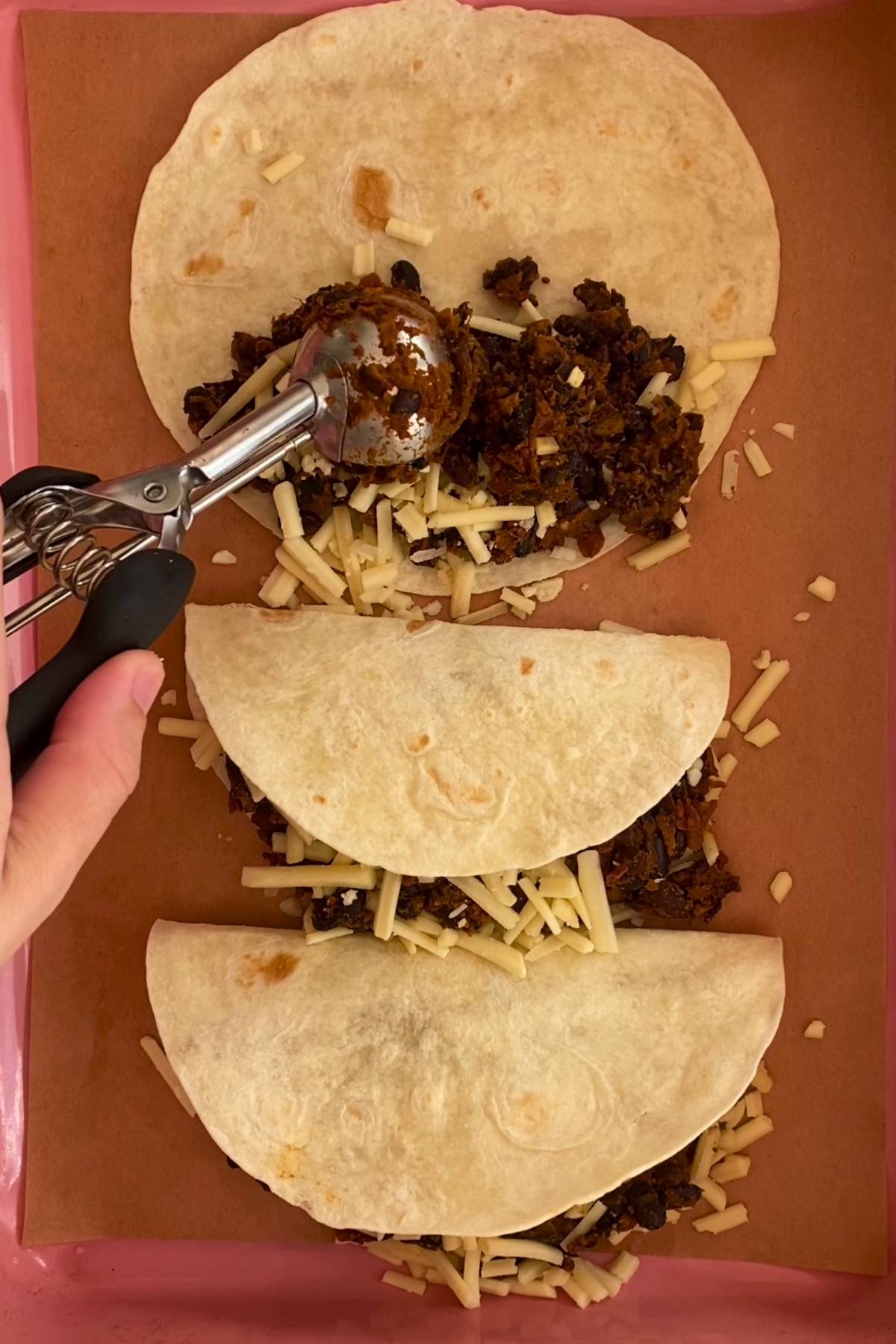 Tortillas filled with mashed beans and shredded cheese before baking.