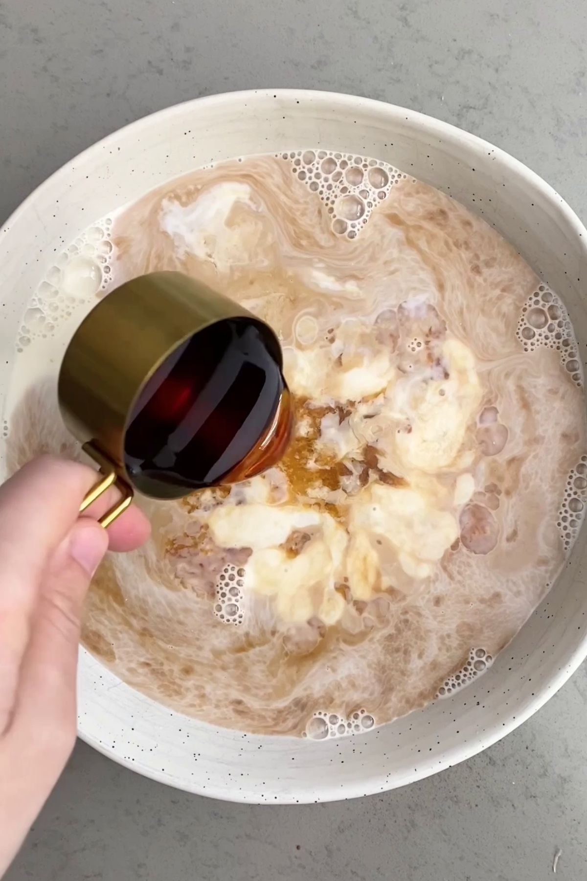Maple syrup being poured into a bowl of plant milk and nut butter mixture.