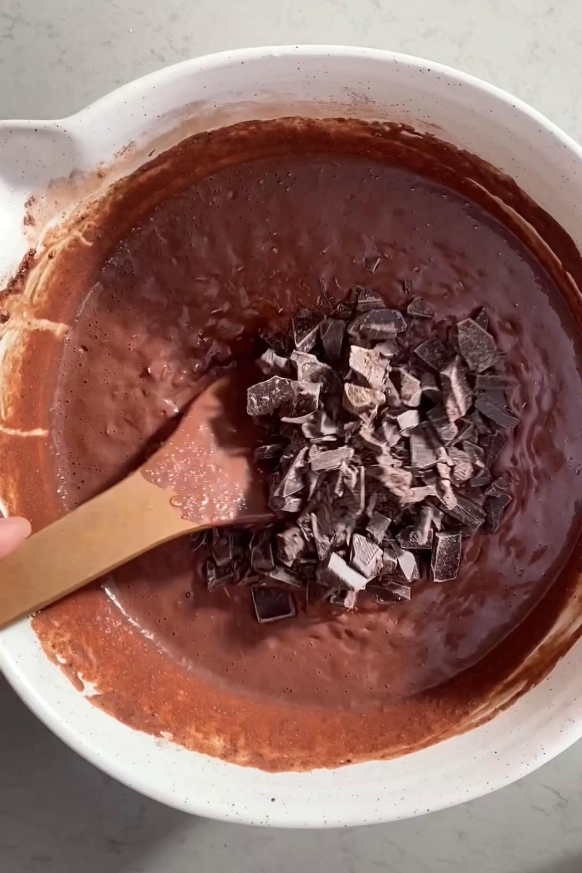 Chopped dark chocolate added to brownie batter in a mixing bowl.