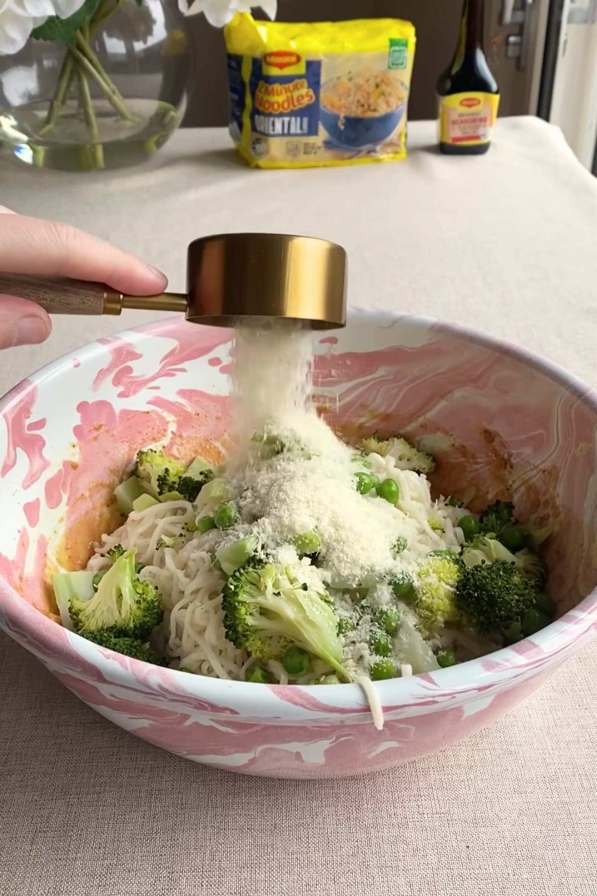 Breadcrumbs being poured over noodles with broccoli and peas in a bowl.