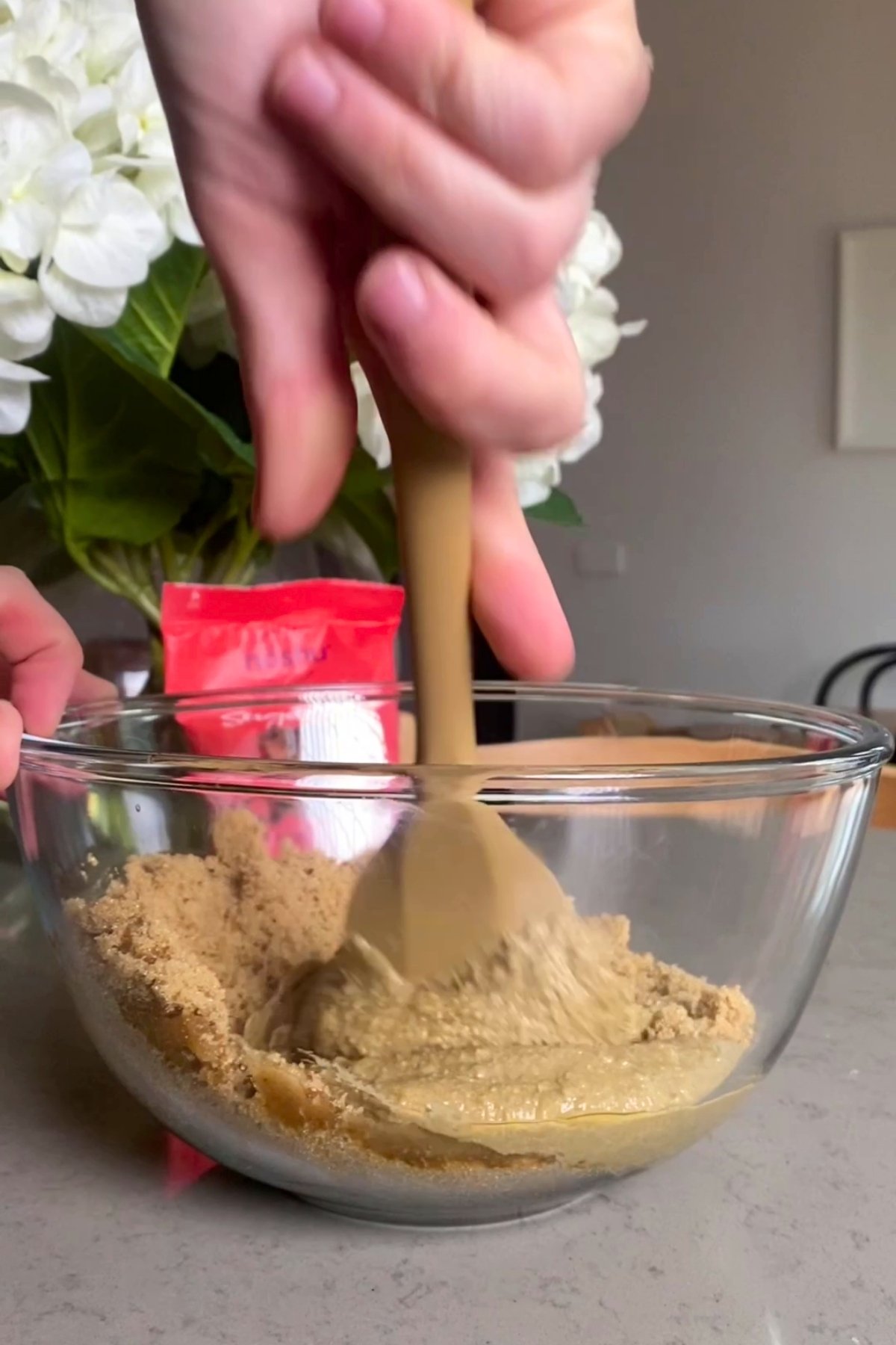 Hand mixing sunflower seed butter and brown sugar in a glass bowl.