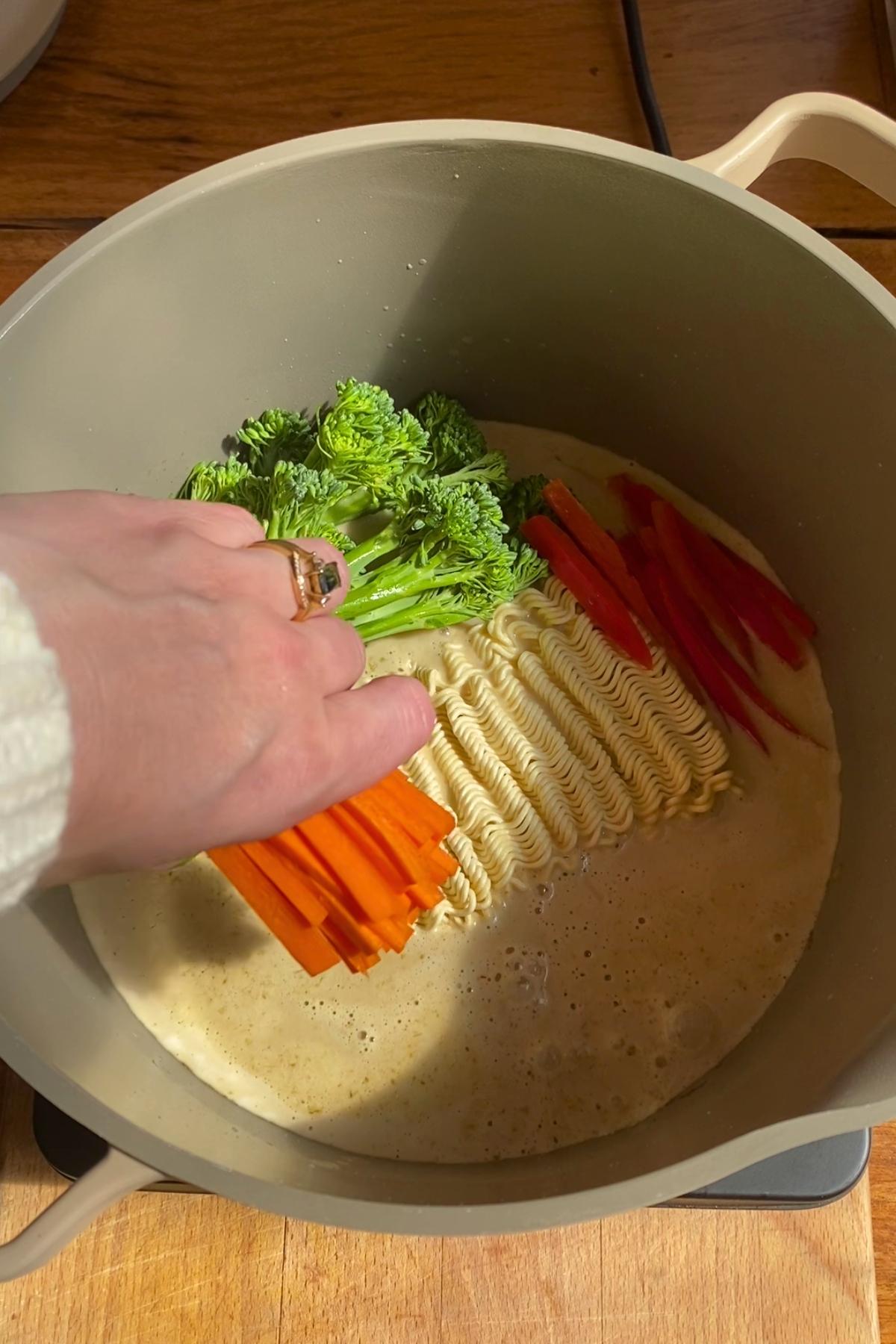 Raw noodles, broccolini, carrot, and red pepper added to broth.