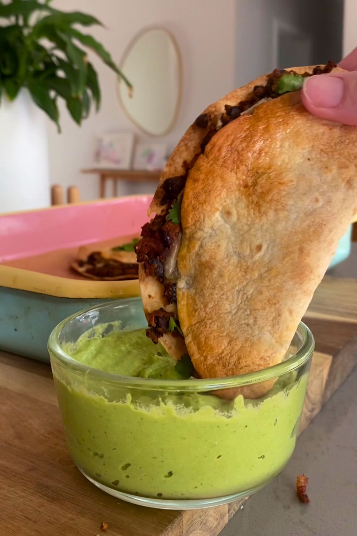 Taco being dunked deeper into a bowl of avocado dip.