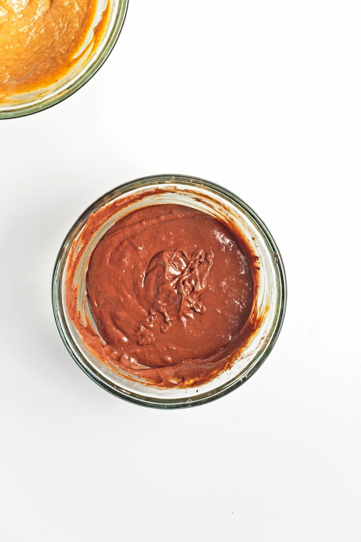 Glass bowl filled with smooth chocolate batter beside pumpkin batter.
