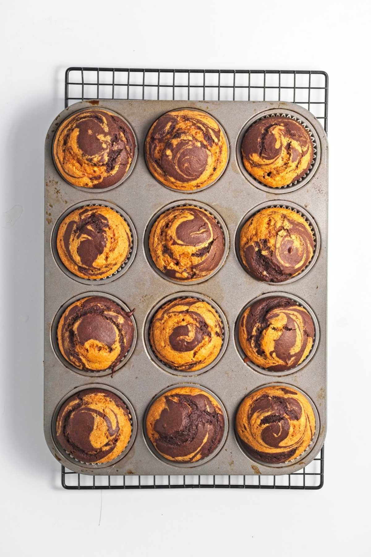 Baked muffins cooling in a tin on a wire rack.