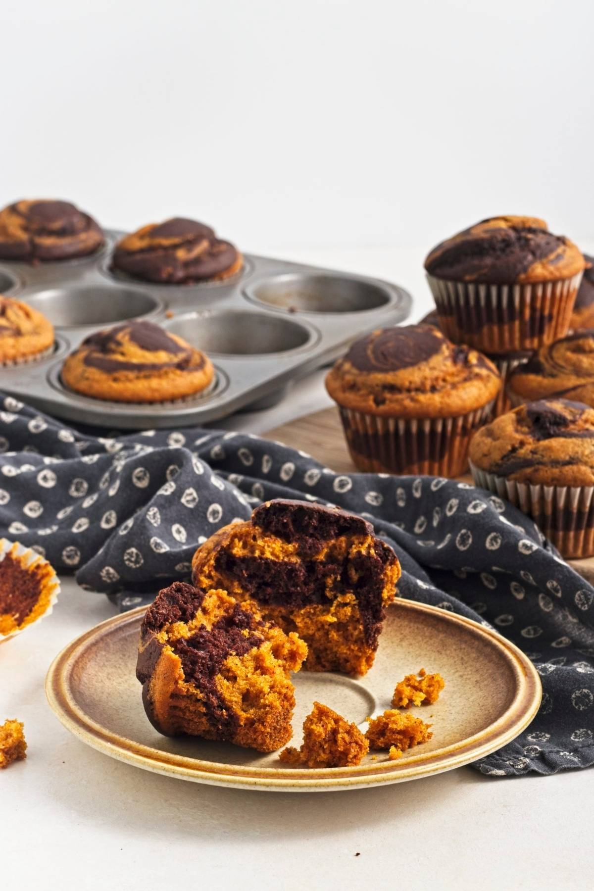 Split muffin on a plate showing pumpkin and chocolate swirls.