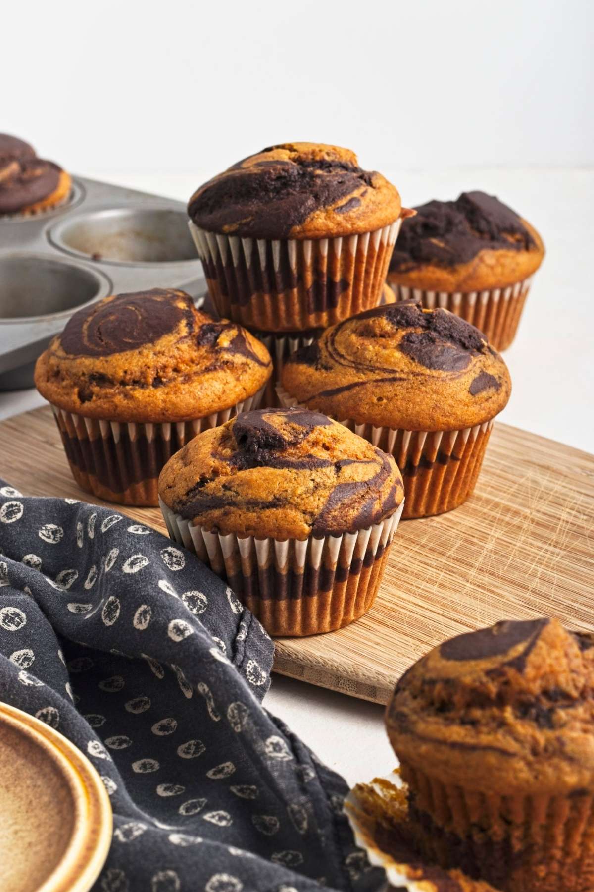 Stack of pumpkin chocolate swirl muffins on a wooden board.