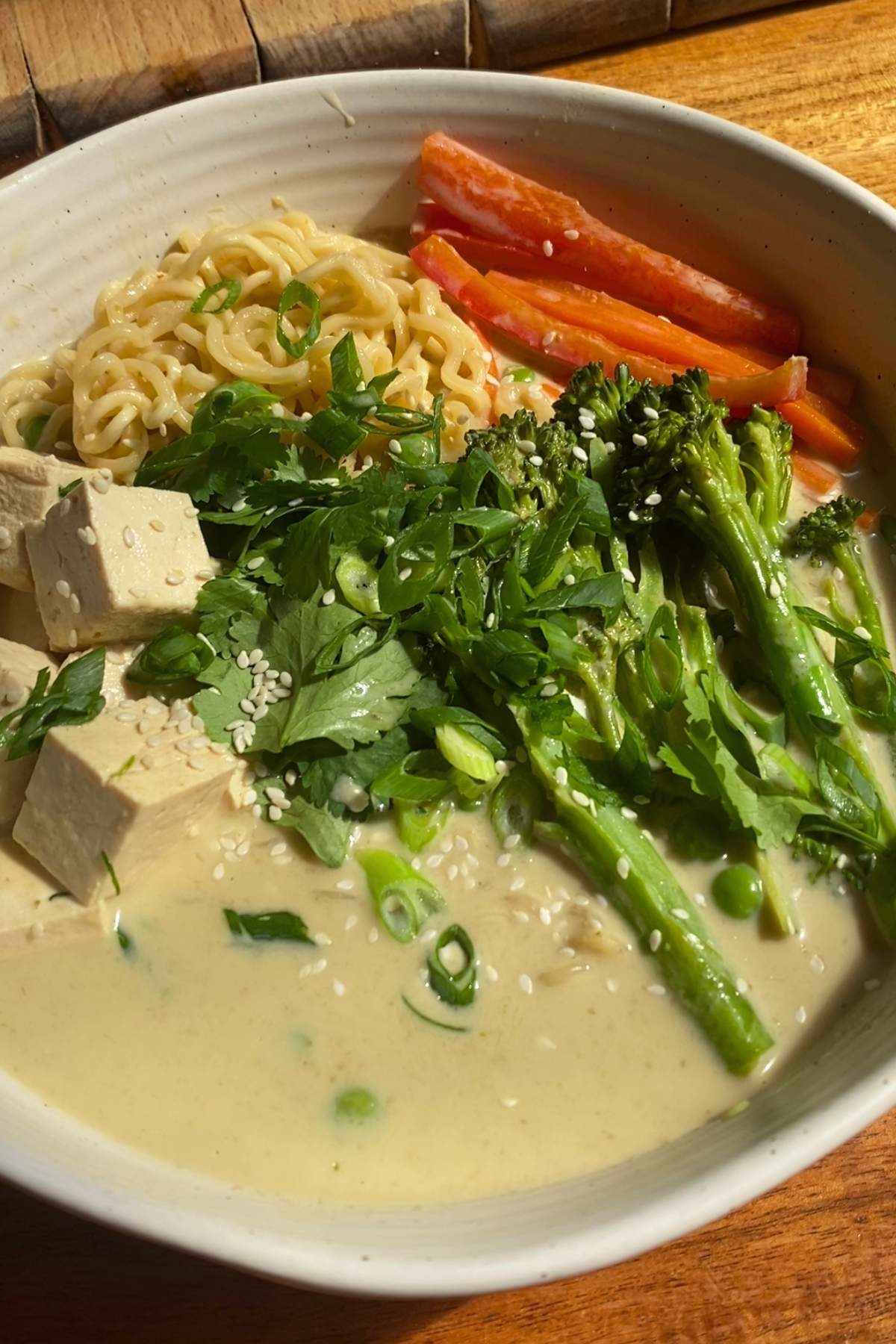 Close-up of noodle bowl with tofu, broccolini, carrots, and fresh herbs.