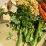Noodle bowl with tofu cubes, broccolini, red peppers, herbs, and sesame seeds.