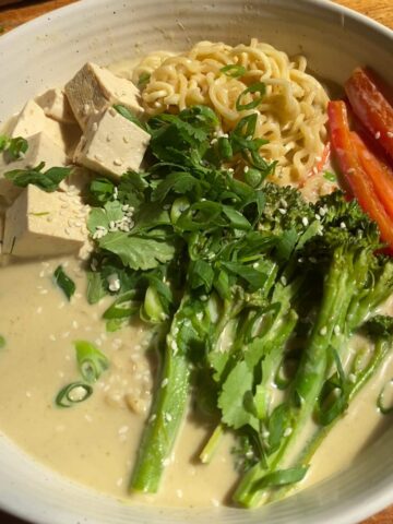 Noodle bowl with tofu cubes, broccolini, red peppers, herbs, and sesame seeds.