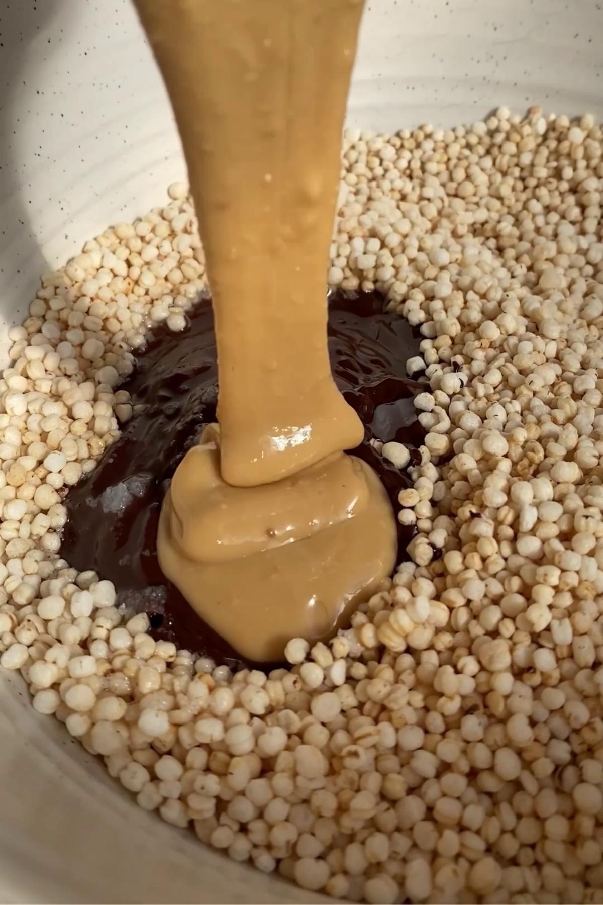 Thick peanut butter being poured into a bowl with melted chocolate and puffed quinoa.