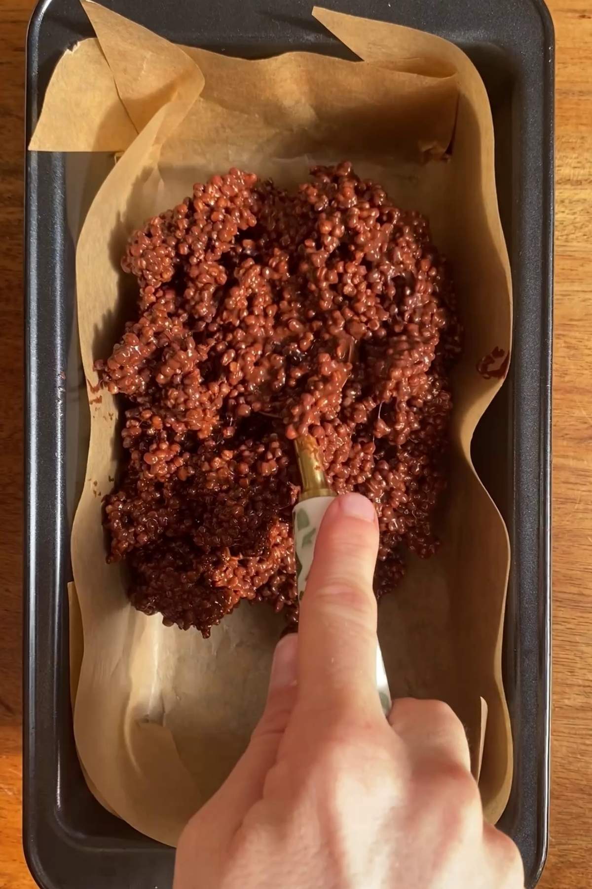Chocolate quinoa mixture being pressed into a parchment-lined loaf pan.