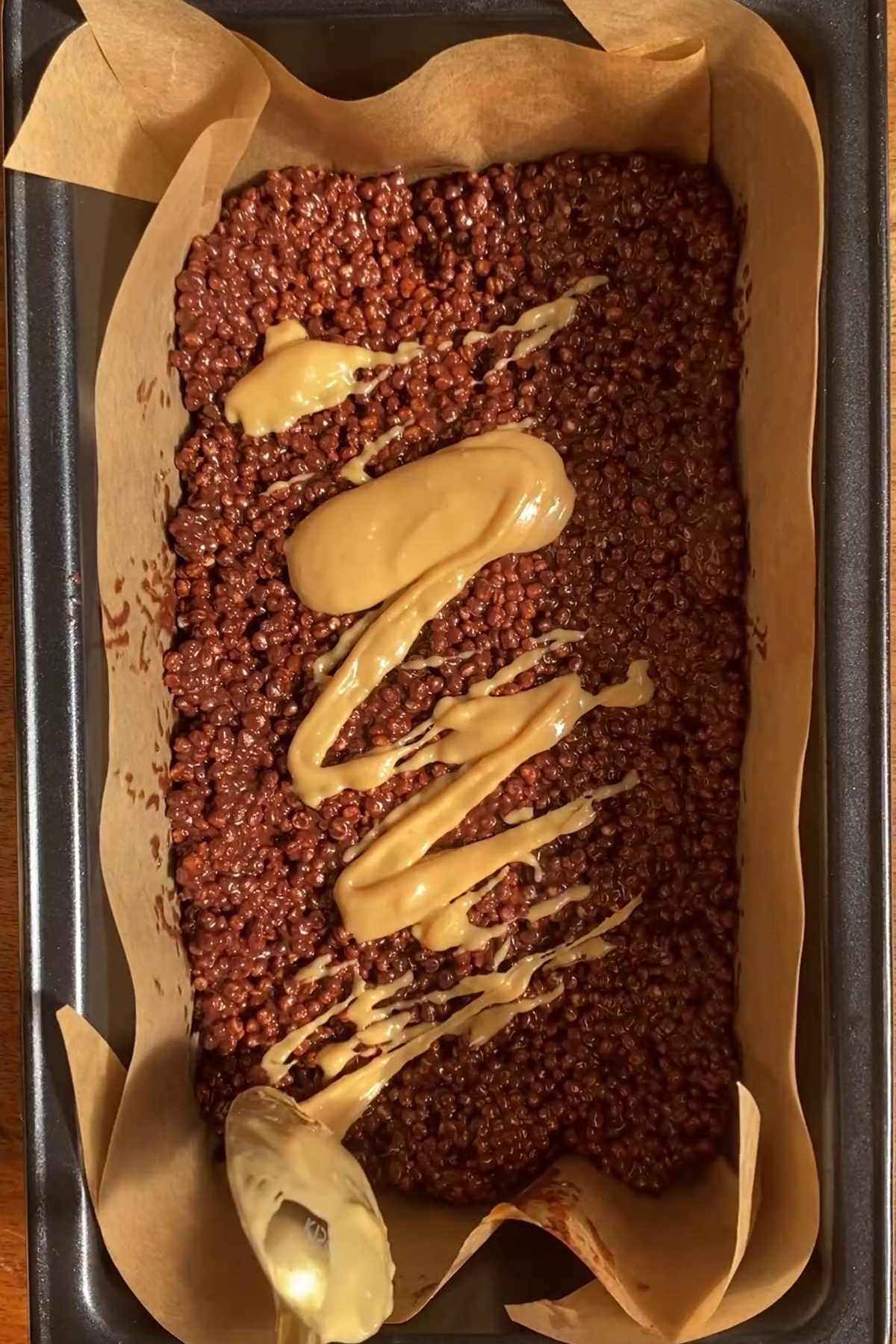 Peanut butter being drizzled over the pressed chocolate quinoa layer.