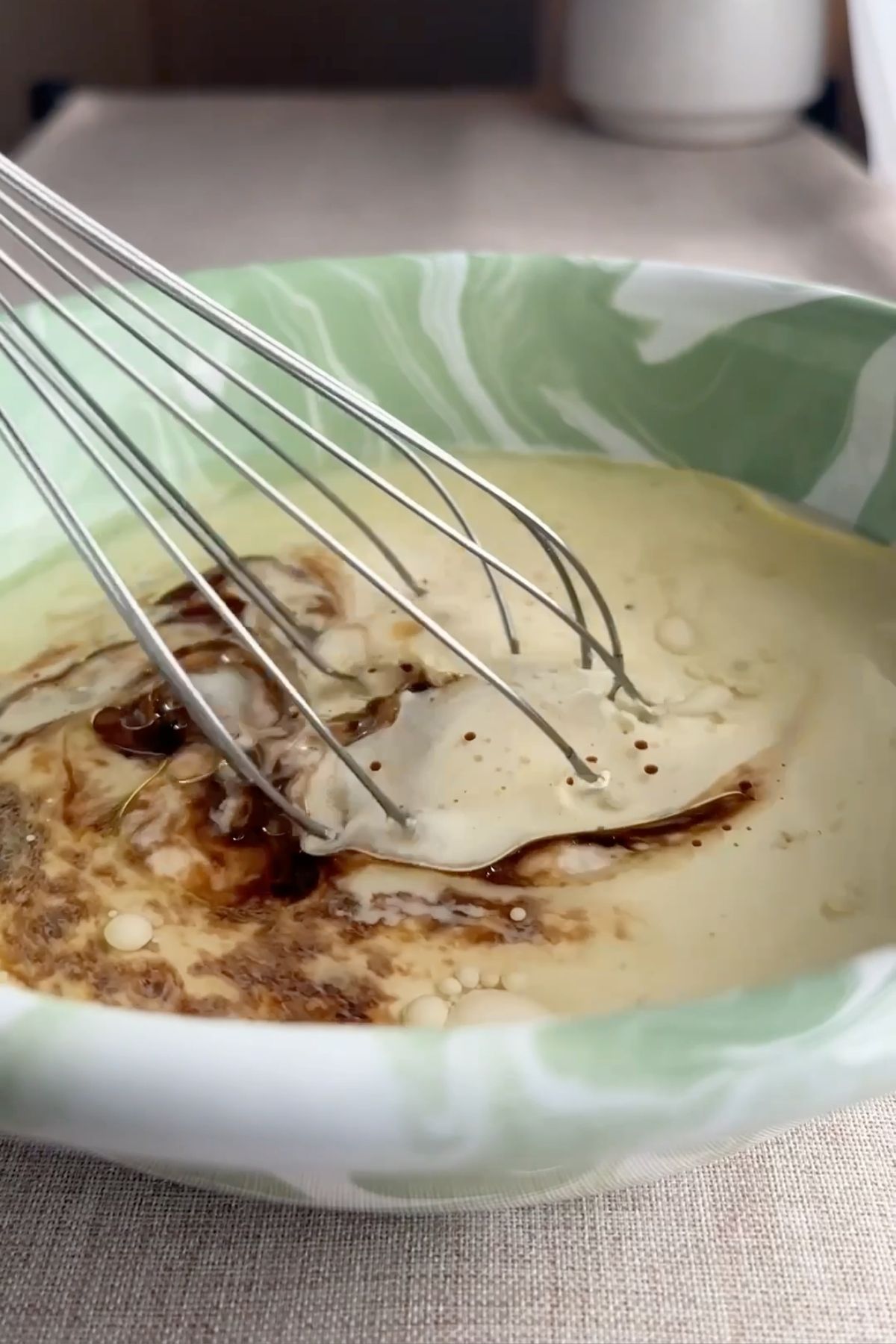 Whisk mixing liquid ingredients in a green marbled bowl.