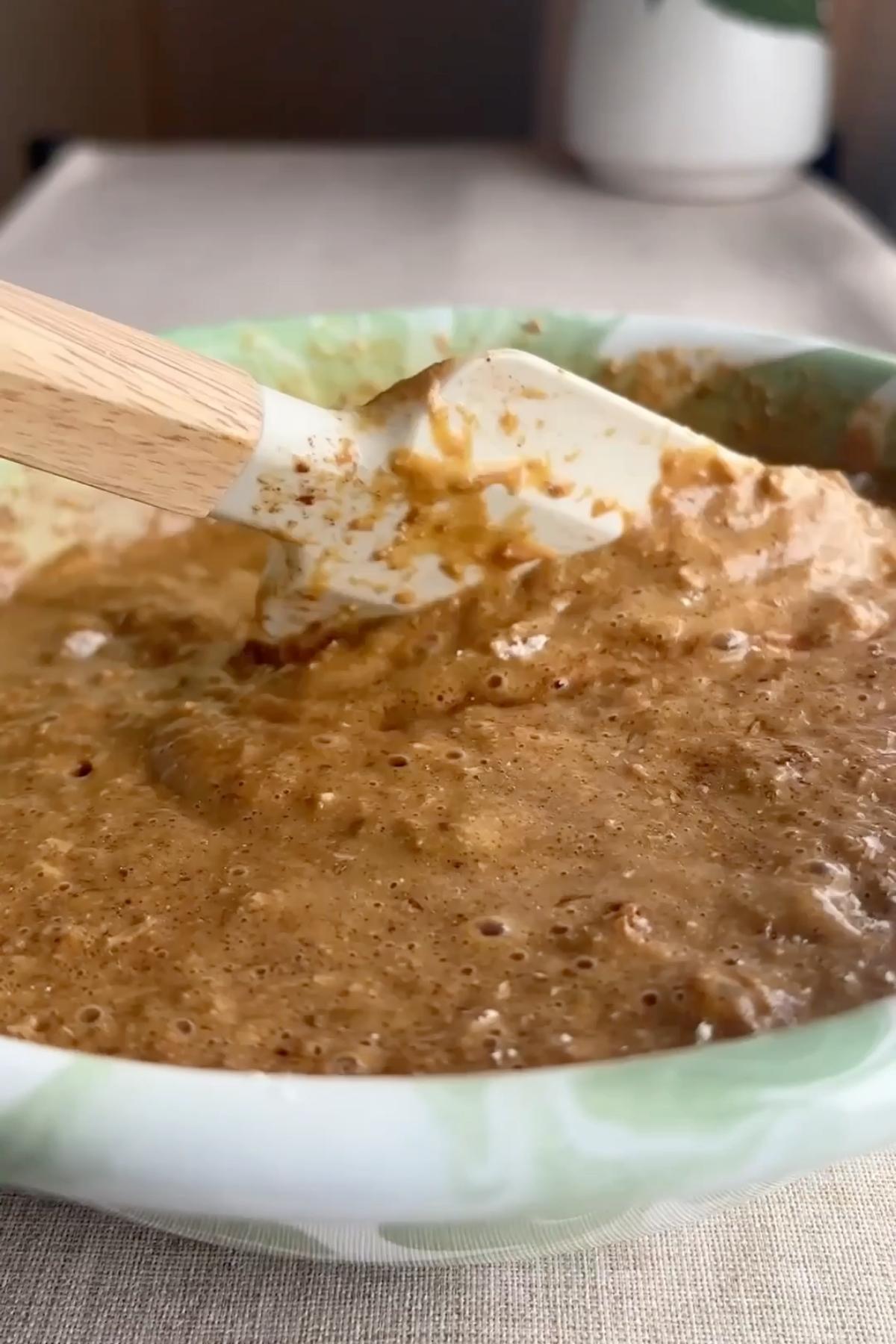 Thick muffin batter being stirred with a spatula in a green marbled bowl.