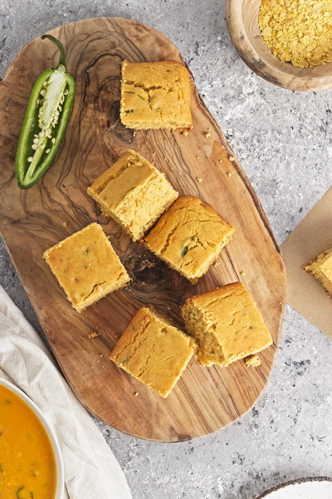 Square pieces of golden cornbread with visible jalapeño slices on a wooden board.