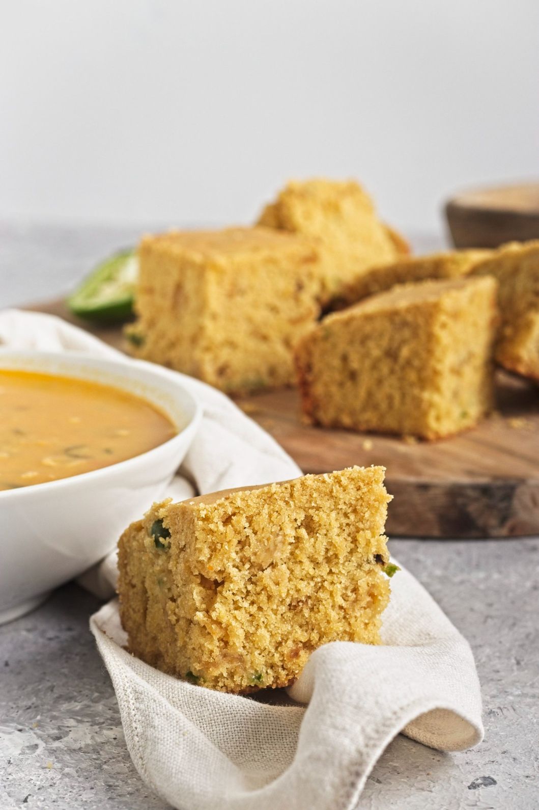 Close-up of a cornbread slice resting on a napkin beside a bowl of soup.