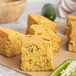Golden slices of cornbread with jalapeño pieces on parchment, showing a soft, crumbly texture and crisp edges.