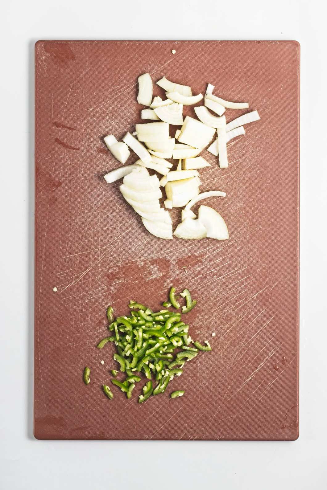 Chopped onion and finely sliced jalapeño arranged on a brown cutting board.