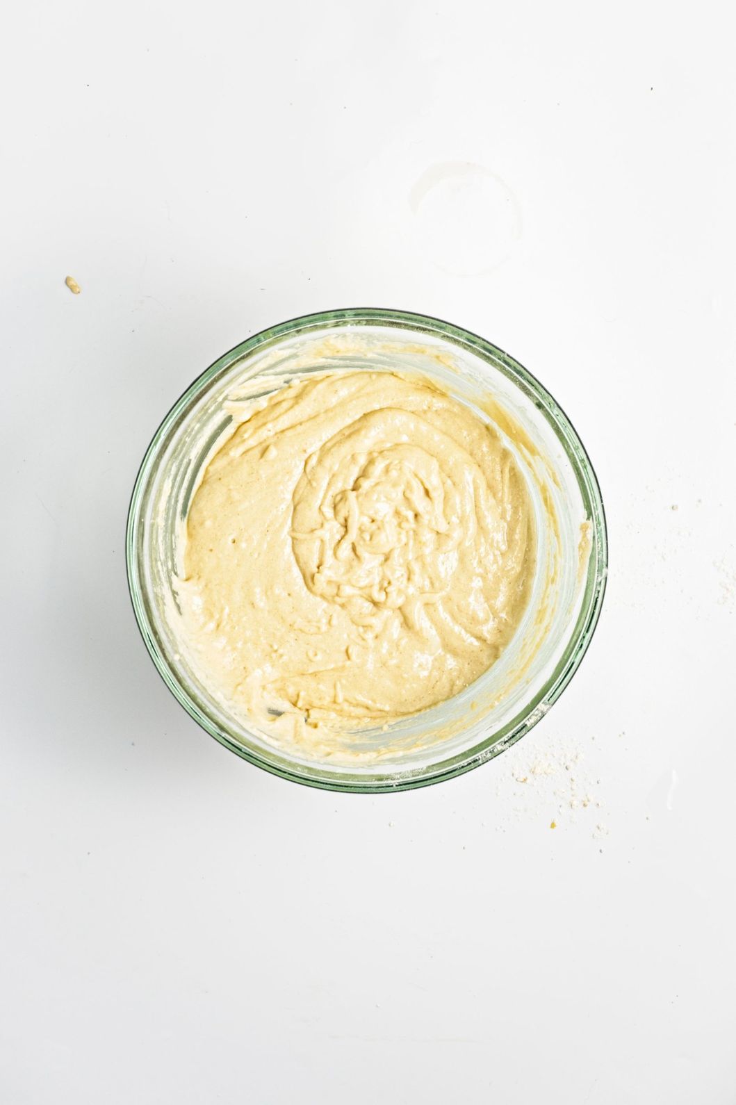 Smooth cornbread batter in a glass bowl on a white surface.
