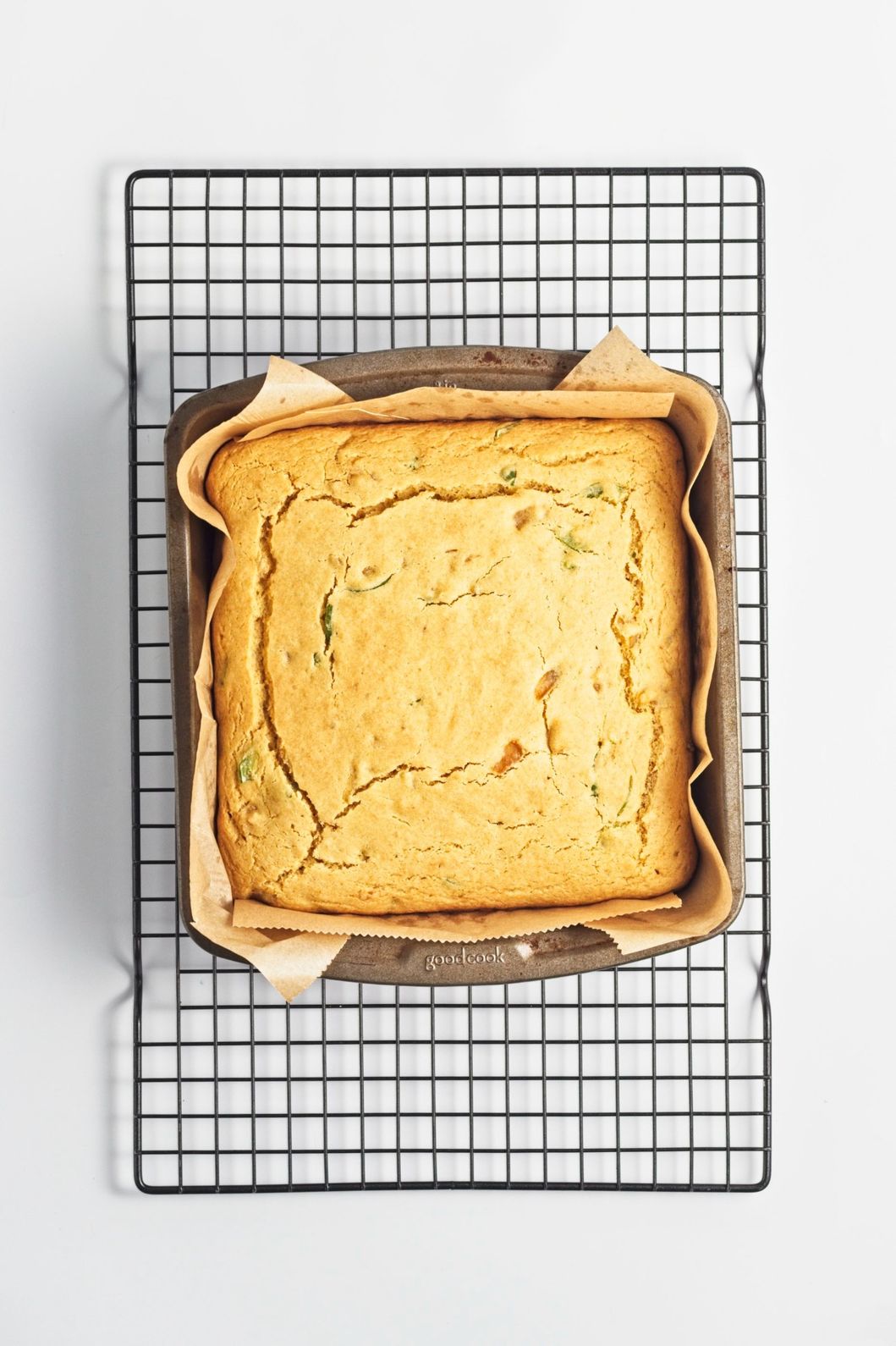 Golden-brown cornbread cooling in a parchment-lined pan on a wire rack.