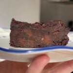 Fudgy slice of chocolate brownie on a small white plate, showing chunks of melted chocolate inside.