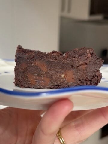 Fudgy slice of chocolate brownie on a small white plate, showing chunks of melted chocolate inside.
