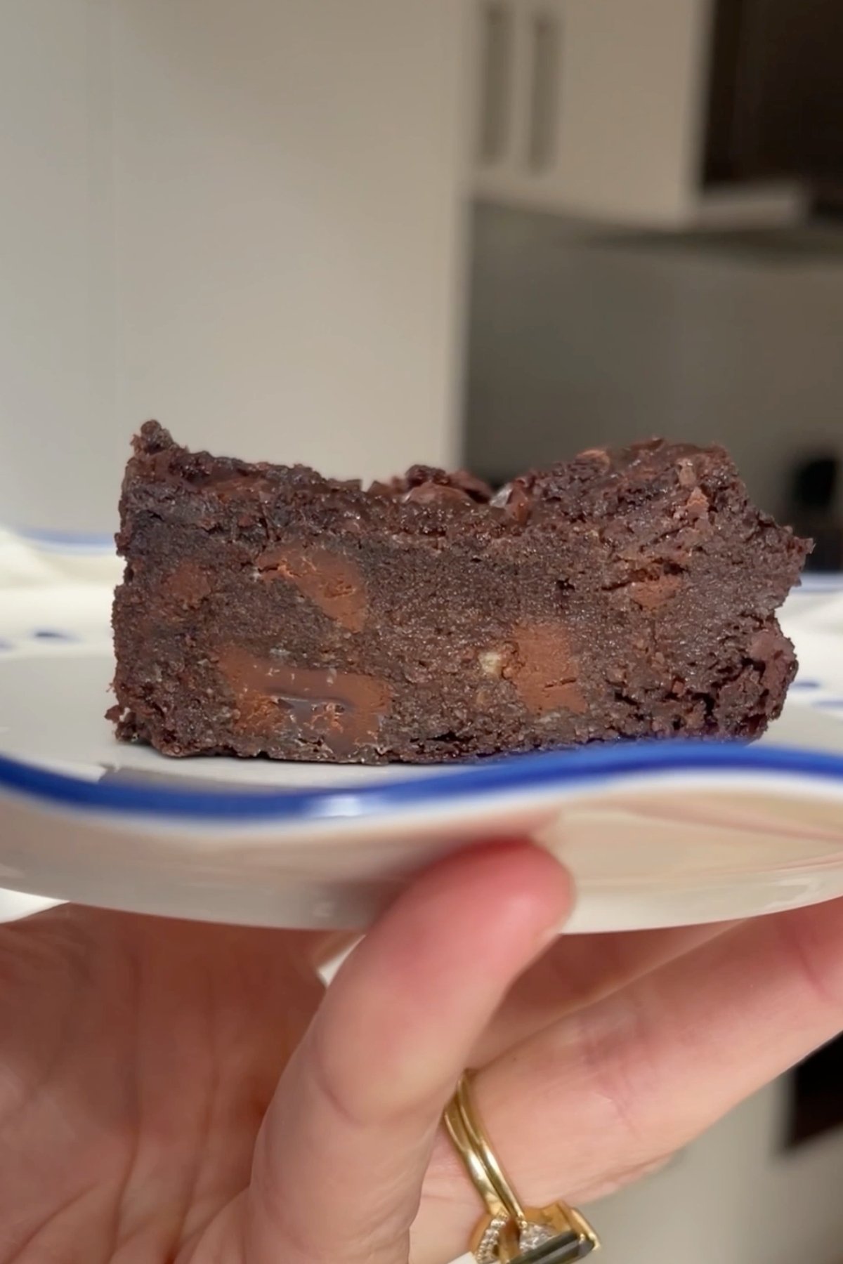 Fudgy slice of chocolate brownie on a small white plate, showing chunks of melted chocolate inside.