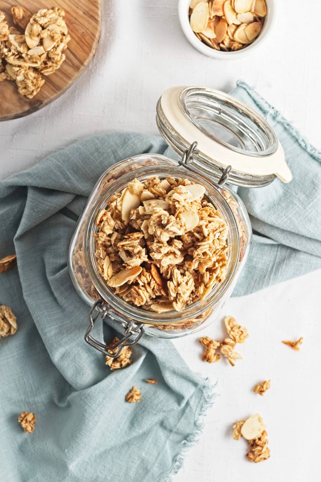 Homemade granola with oats and almonds stored in a glass jar on a light blue cloth.
