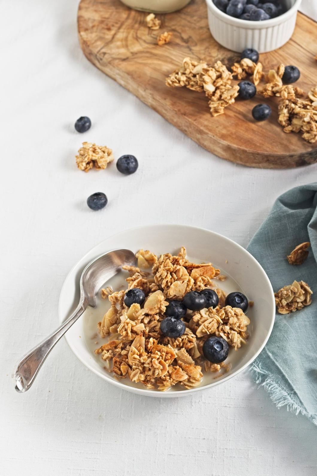 Bowl of granola with blueberries and milk on a white tablecloth.