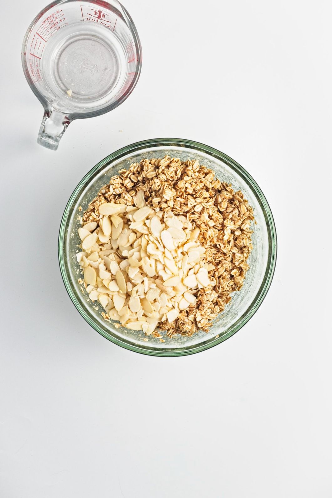 Oat and almond mixture combined with syrup mixture and sliced almonds in a glass bowl.