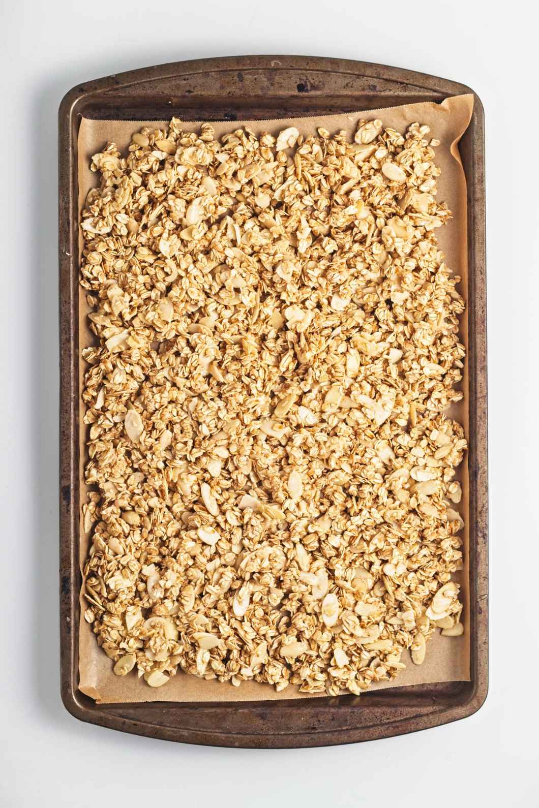 Granola mixture spread evenly on a parchment-lined baking tray before baking.