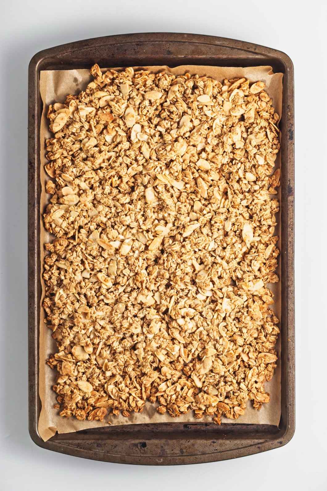 Baked golden granola cooling on a parchment-lined tray.