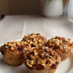 Close-up of muffins topped with oats and small apple pieces on a white plate.