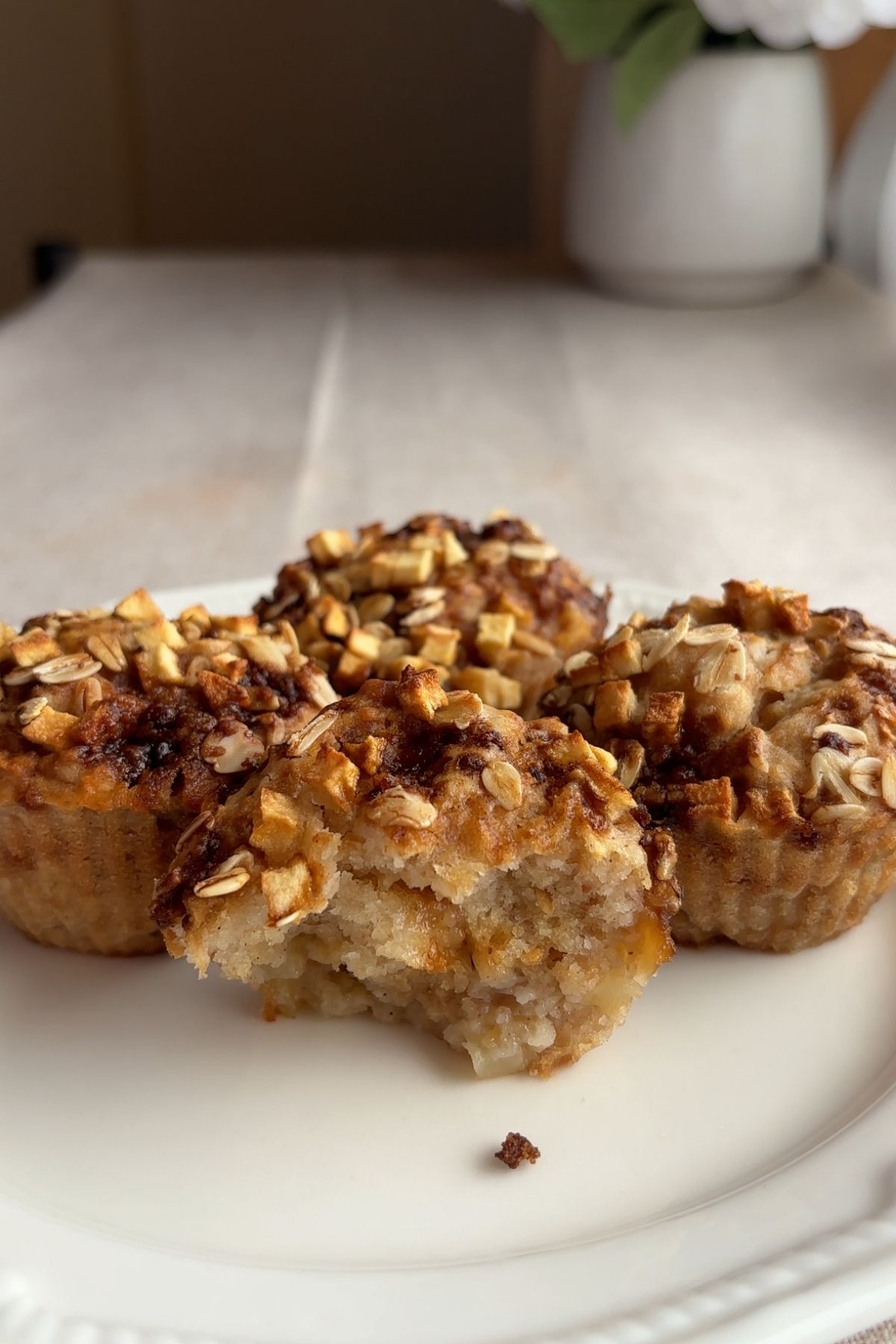 Muffins topped with diced apple and oats on a plate, with one muffin bitten to show the soft interior.